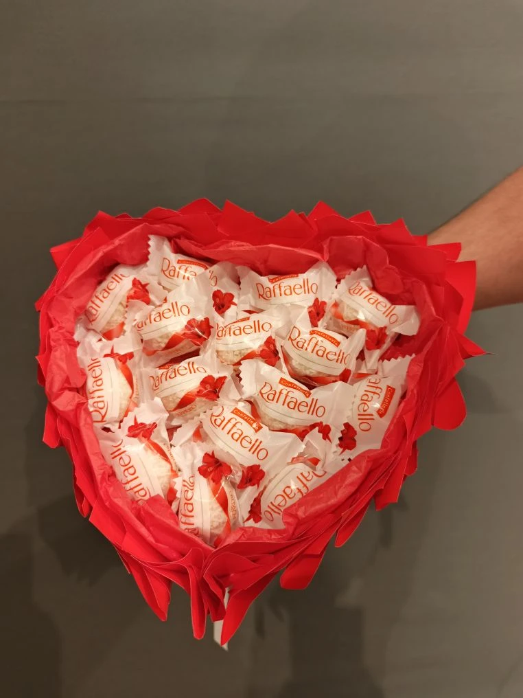 Сладкий букет № 10 в форме сердца: 15 конфет Raffaello, украшенные ярко-красной упаковкой и бумагой тишью. Дополнен белой атласной лентой.
                     Основа — пенопласт в форме сердца, ручка из бамбуковых шпажек. Трогательный сладкий подарок в Коломне